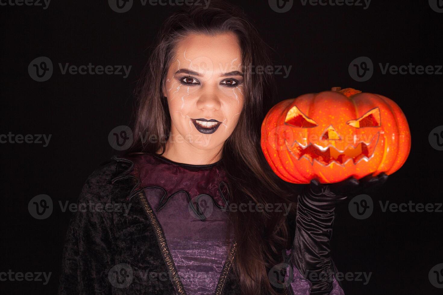 Lady in witch costume holding a pumpkin over black background for halloween. photo