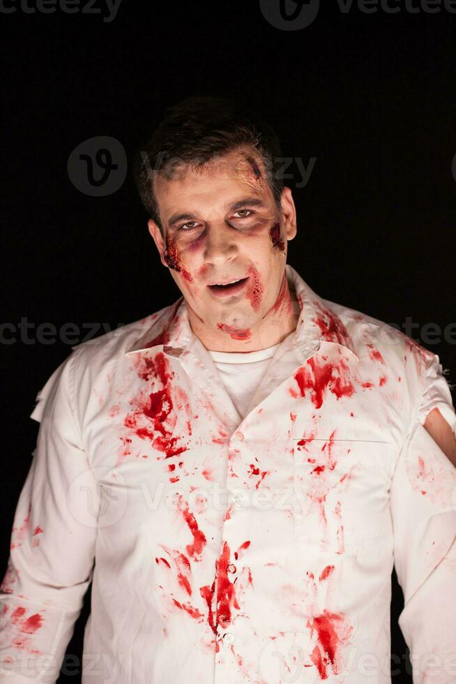 Scary zombie with blood on him after a murder over black background. Halloween outfit. photo