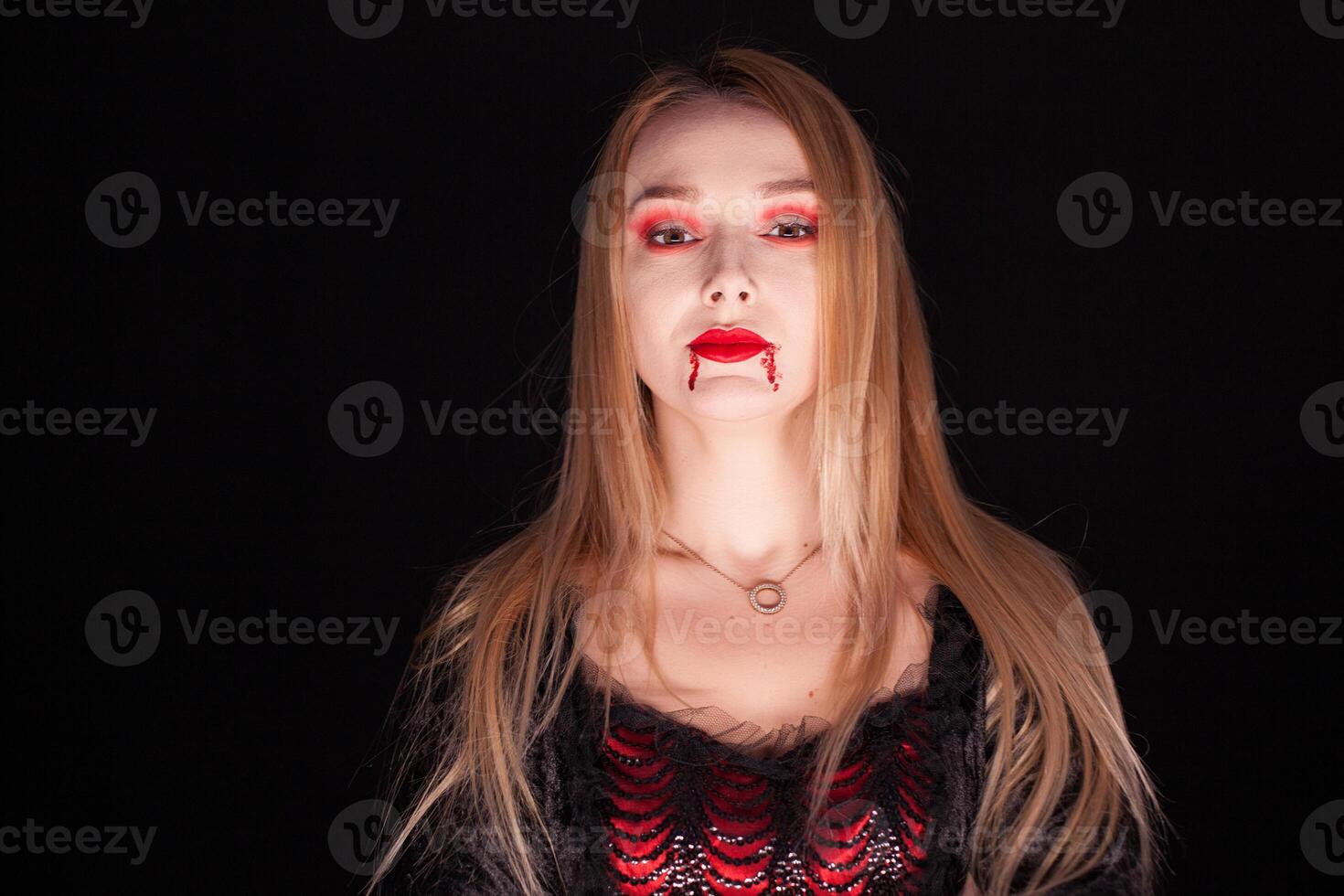 Beautiful blond woman dressed up like a vampire over black background. photo