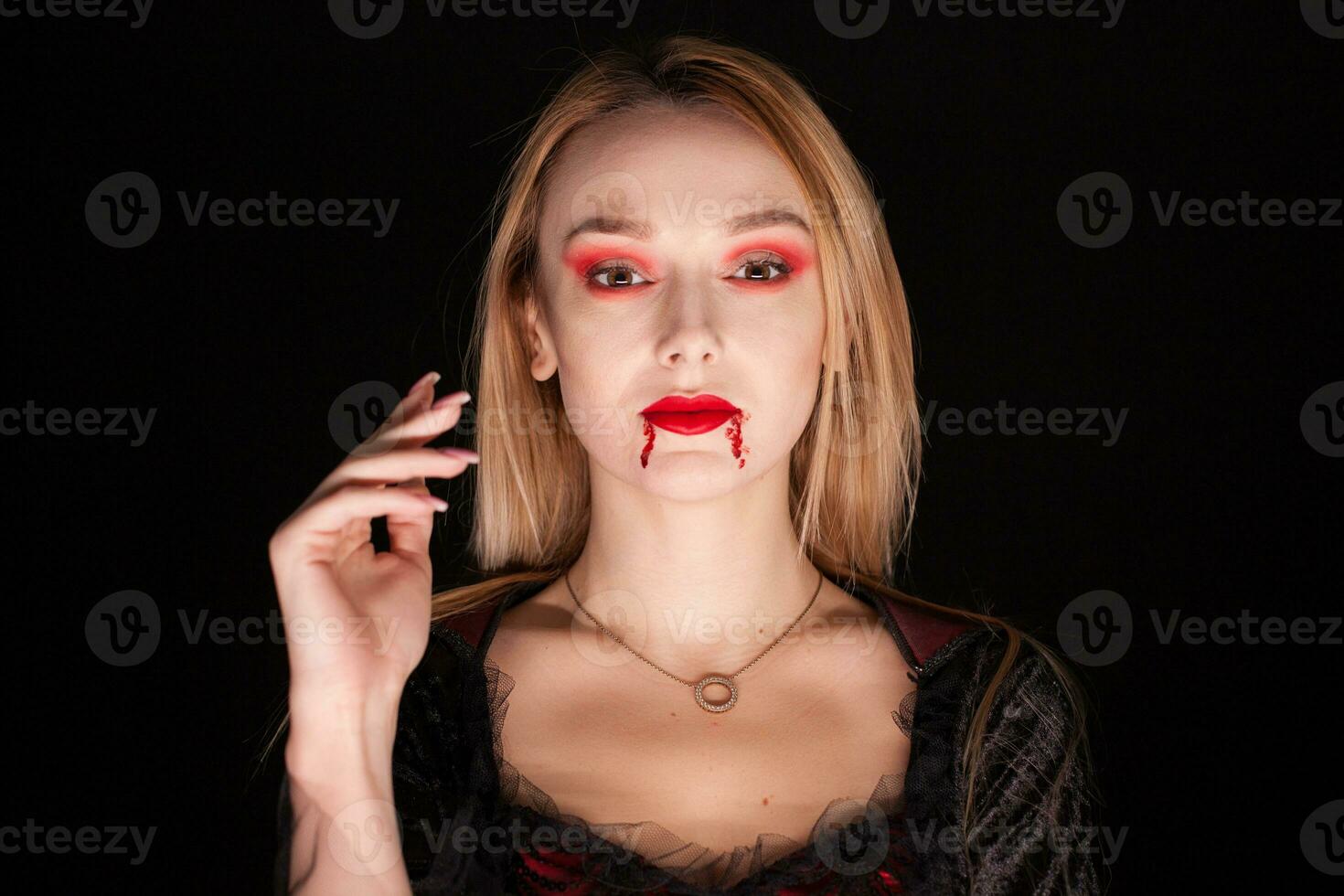 Portrait of beautiful vampire woman over black background. Attractive vampire. photo