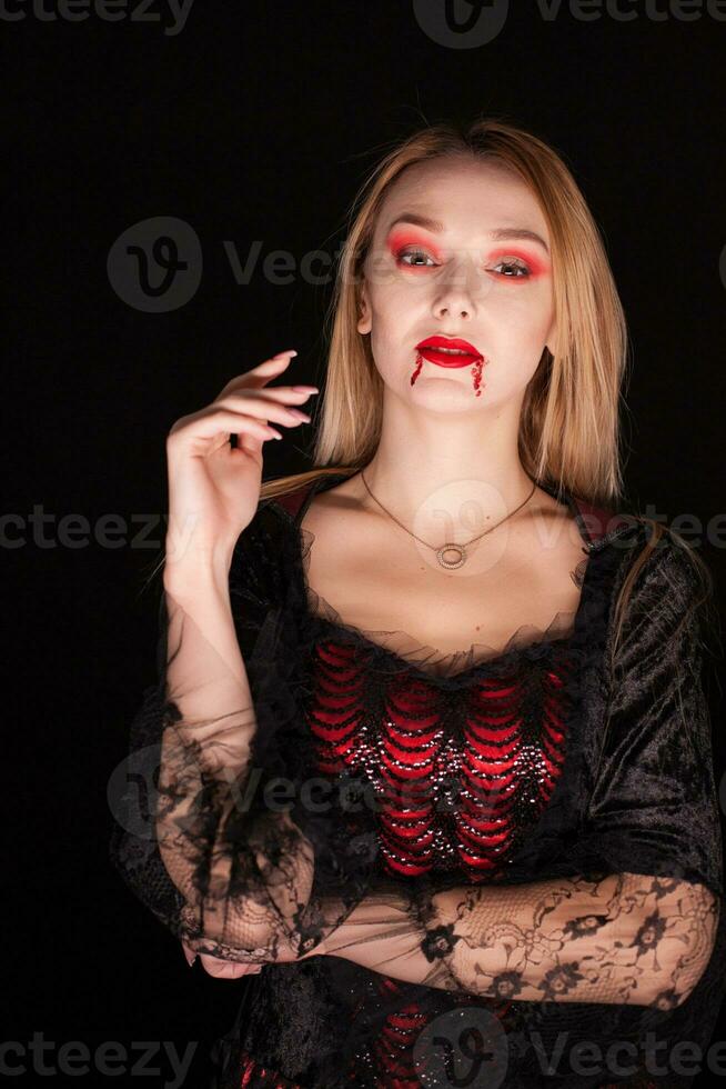 joven bonito mujer con sangre en su labios vestido arriba me gusta un vampiro para Víspera de Todos los Santos terminado negro antecedentes. foto