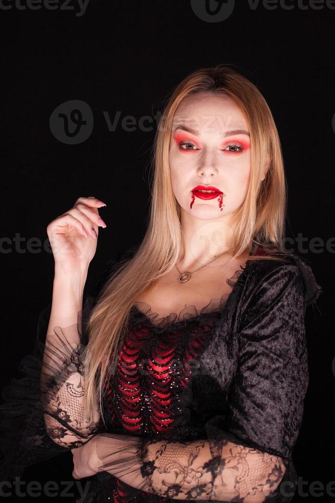 Caucasian girl dressed up like a vampire for halloween over black background. photo