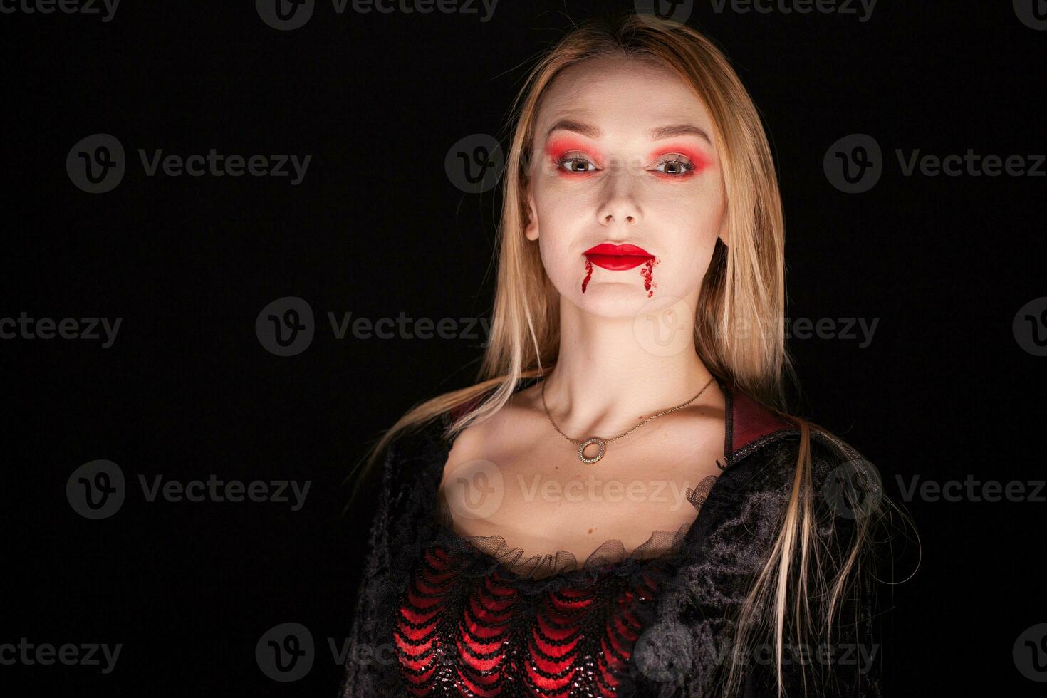 Beautiful vampire woman with dripping blood over black background. photo