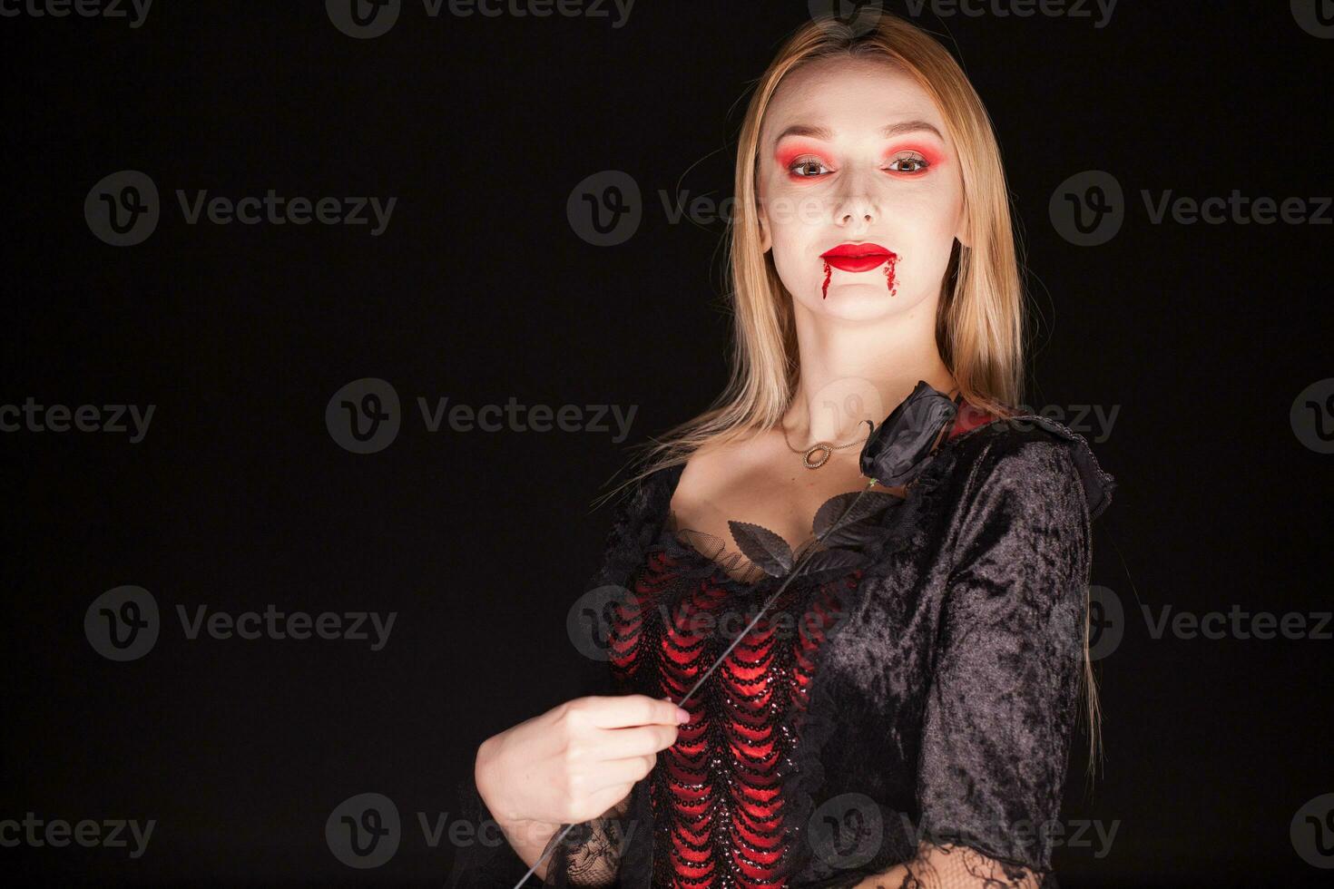 Woman wearing a vampire costume with a rose over black background. photo