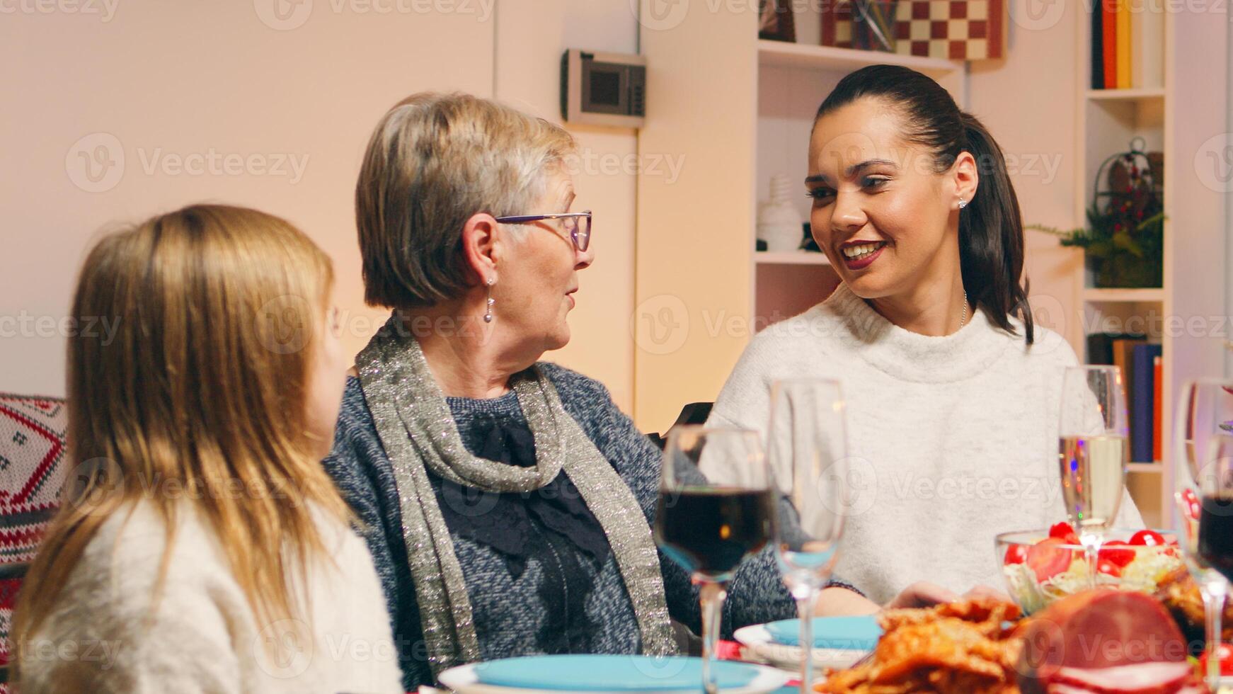Grandmother talking with her daughter and granddaughter at family reunion for christmas celebration. Traditional festive christmas dinner in multigenerational family. Enjoying xmas meal feast in decorated room. Big family reunion photo