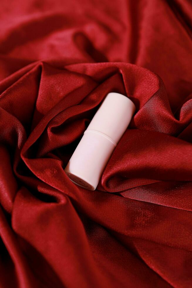 Lipstick on bright scarlet silk or maroon fabric background with soft folds, realistic cosmetic. Beauty Product. photo
