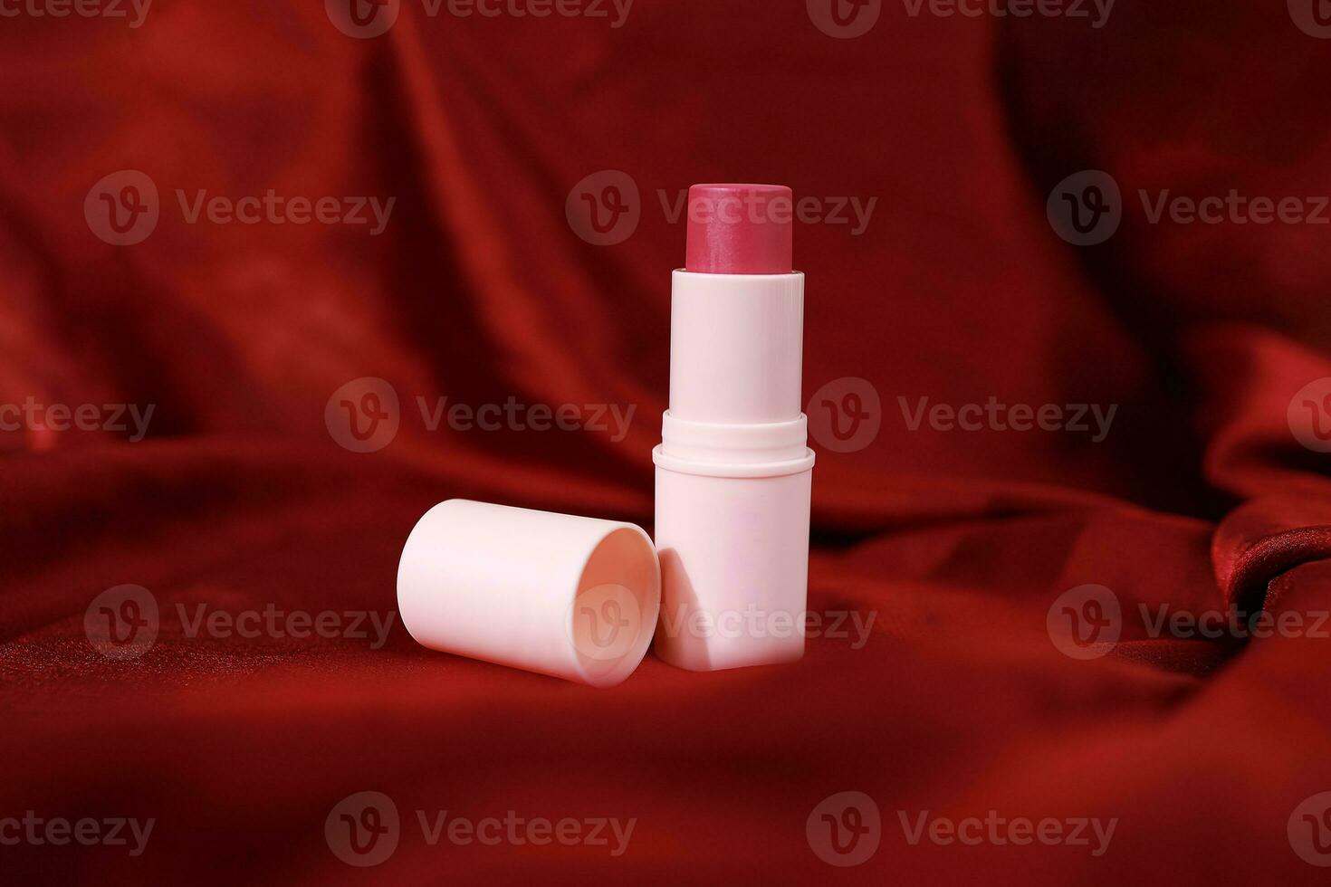 Lipstick on bright scarlet silk or maroon fabric background with soft folds, realistic cosmetic. Beauty Product. photo