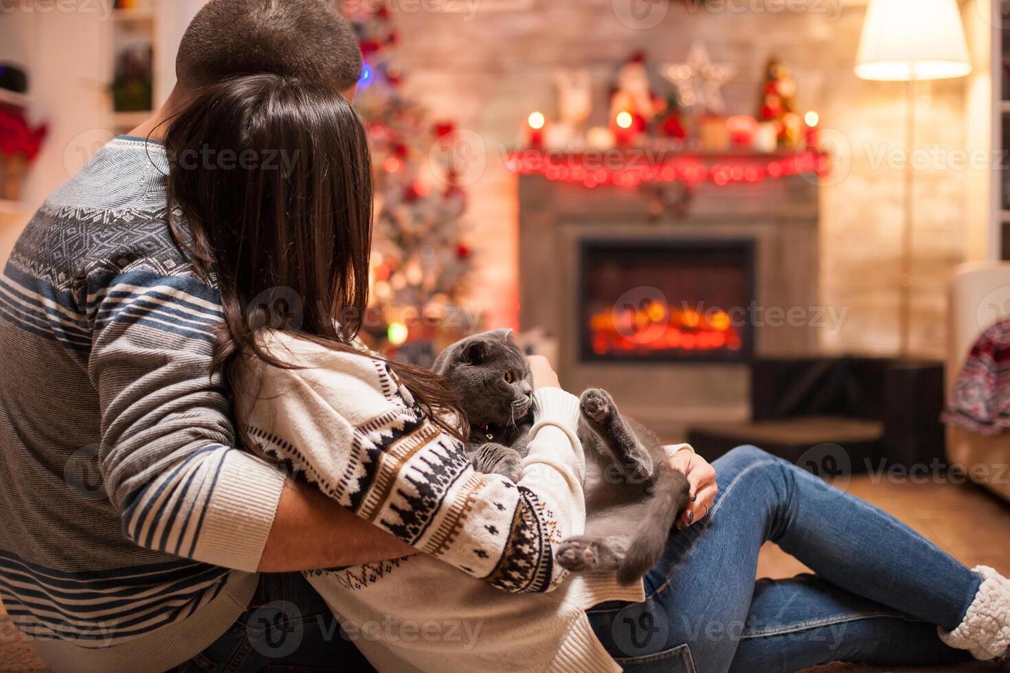 Loving couple and their scottish fold celebrating christmas enjoying the warm of fireplace. photo