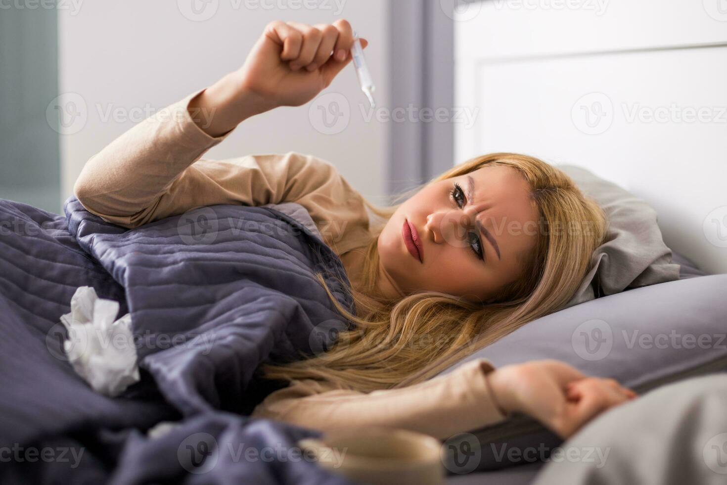 Exhausted woman having fever and checking temperature. photo