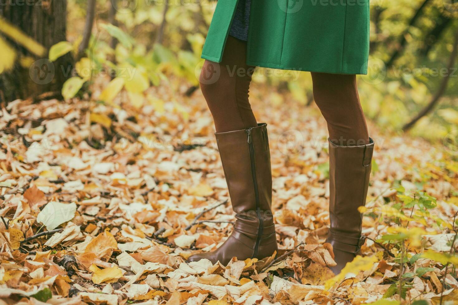 Close up photo of woman in boots surrounded with fall leaveswhile spending time in the park.