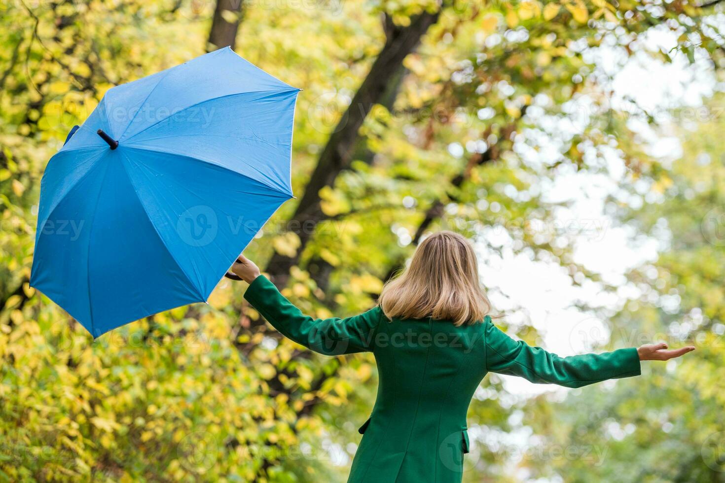 Woman  with her arms outstretched holding umbrella while standing in the park. photo