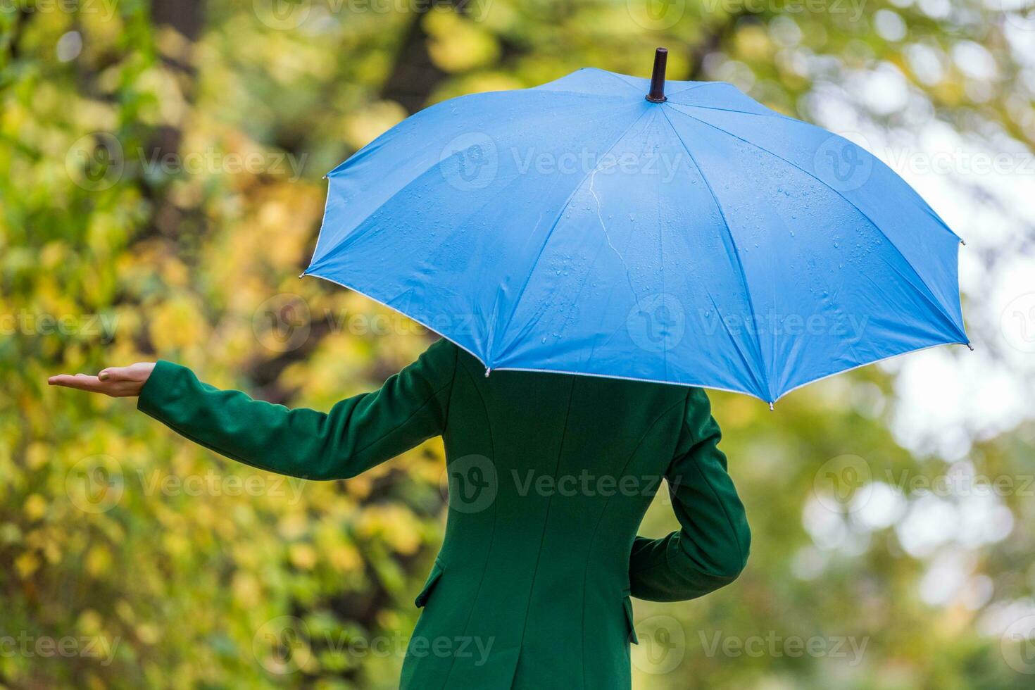 Woman holding blue umbrella and checking for rain while standing in the park. photo