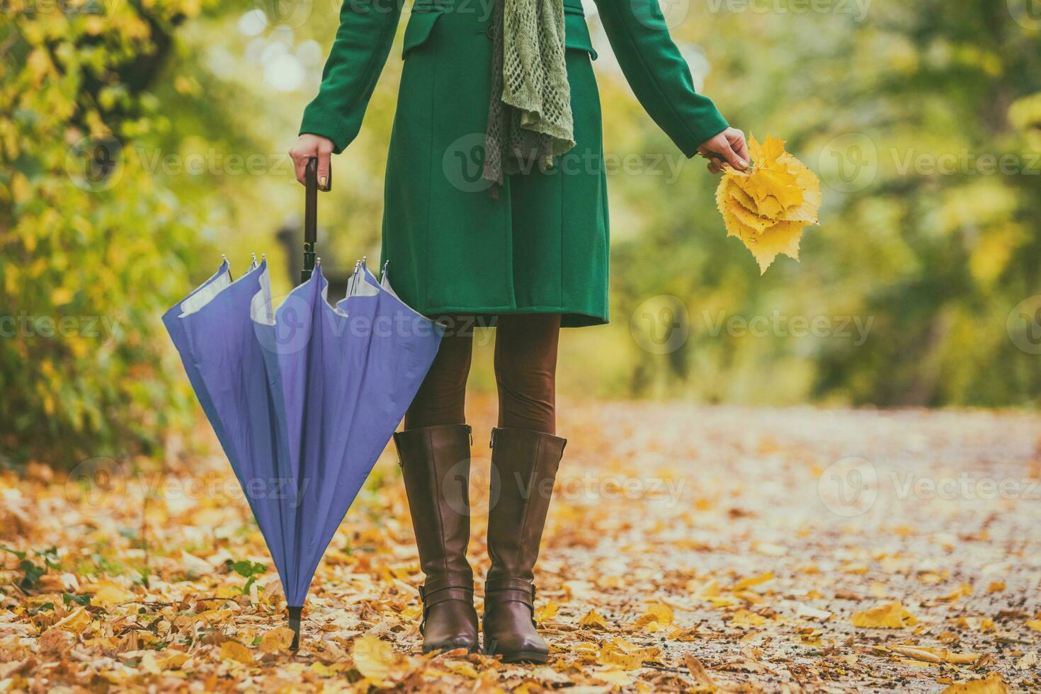 Woman in boots holding umbrella and fall leaves while standing in the park. photo