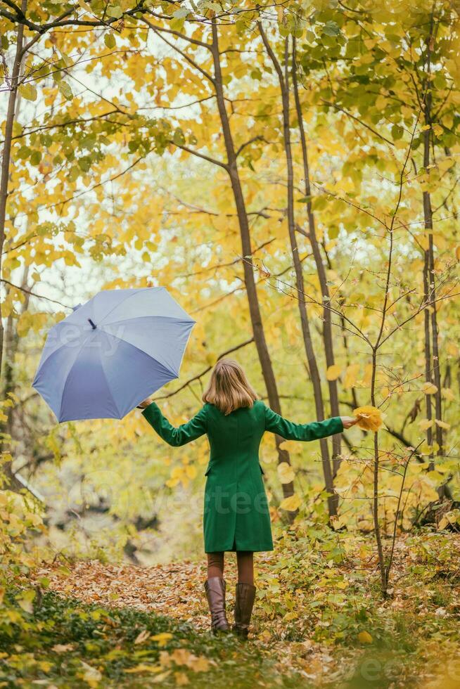 Woman holding umbrella and fall leaves while standing in the park. photo