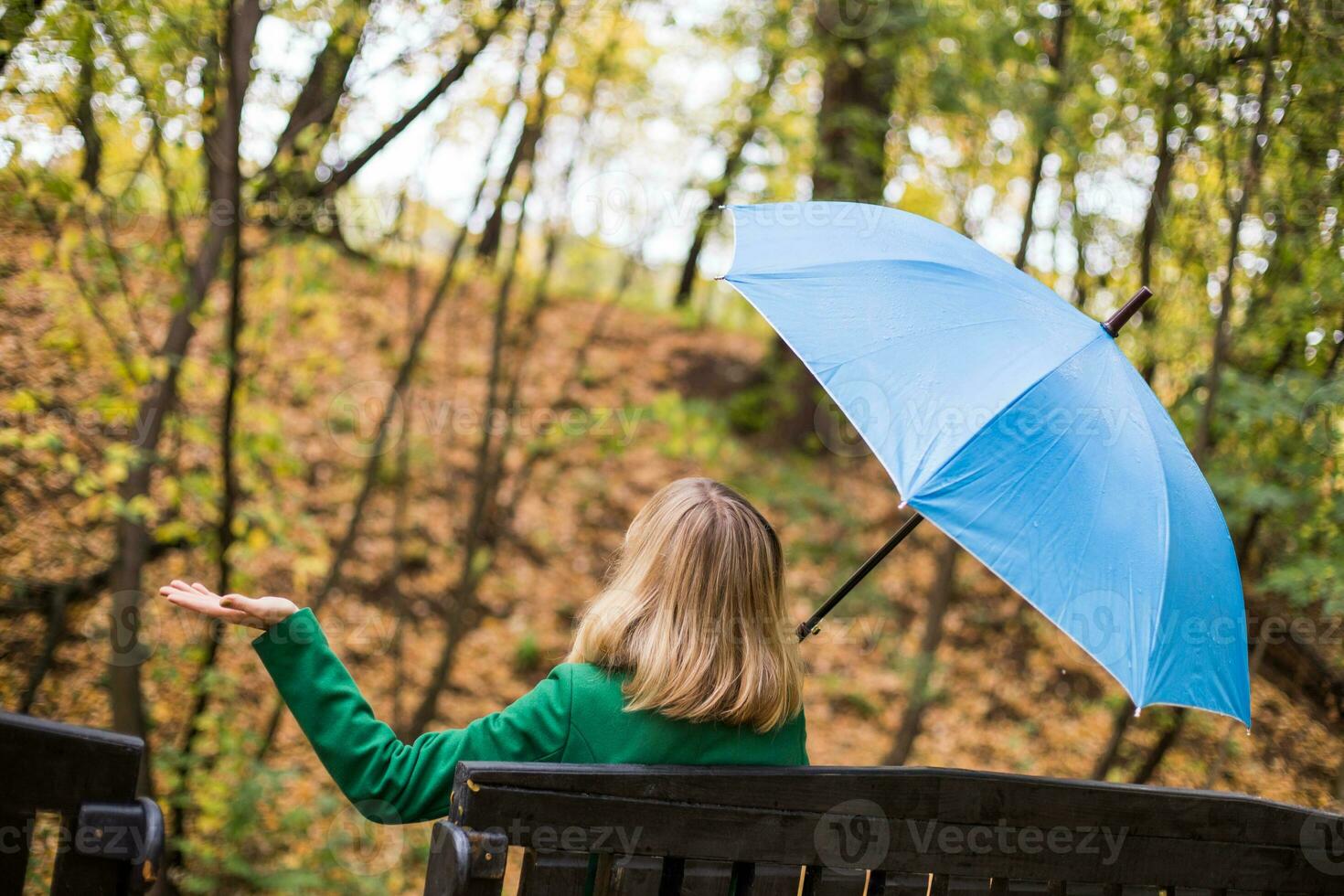 Woman holding blue umbrella and checking for rain while sitting in the park. photo