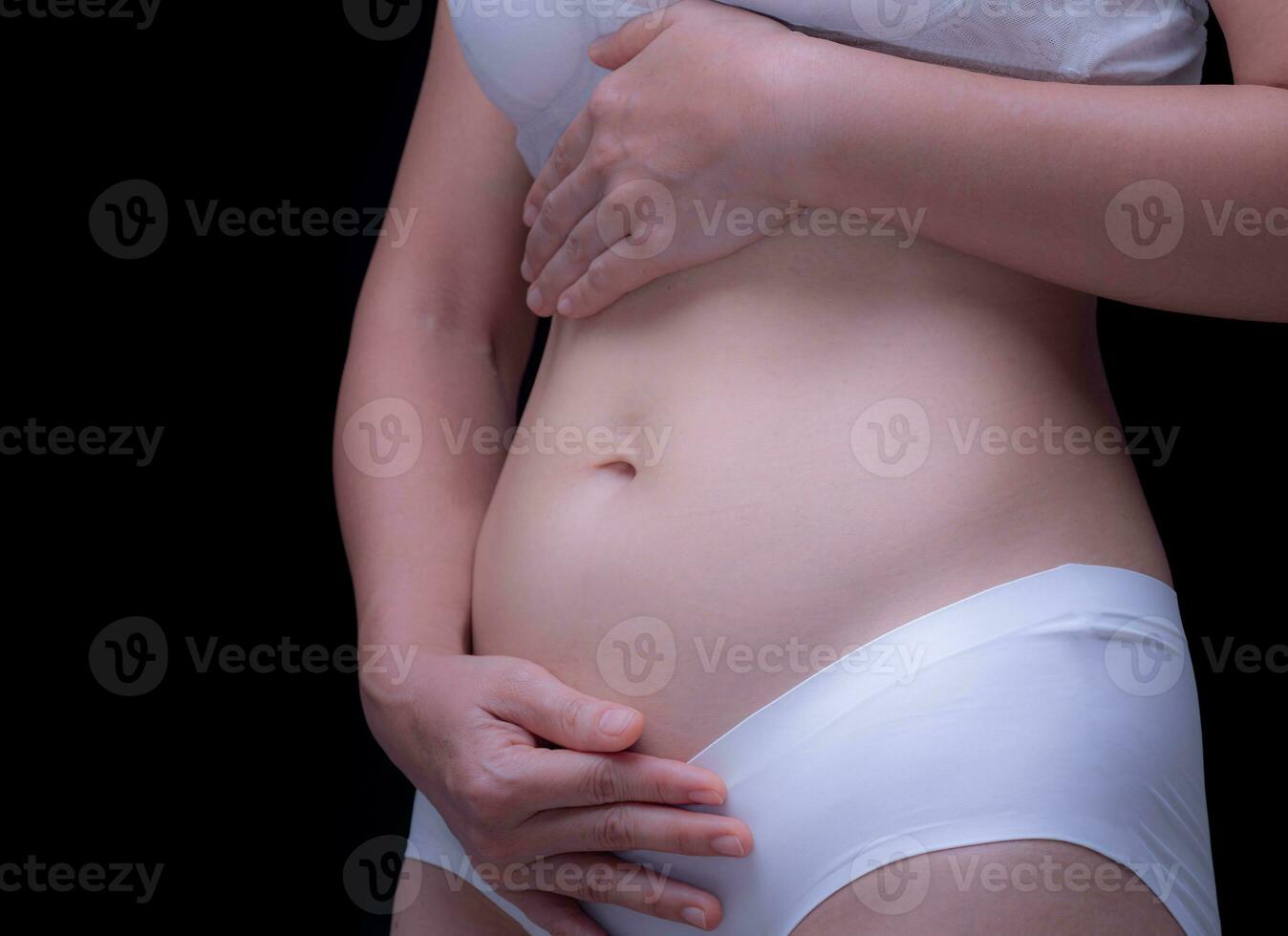 Health concept. Pregnancy. Mother used both hands to support her growing belly. from early pregnancy. First-trimester pregnancy or baby belly 8 weeks or 2 months. Woman on black background. photo