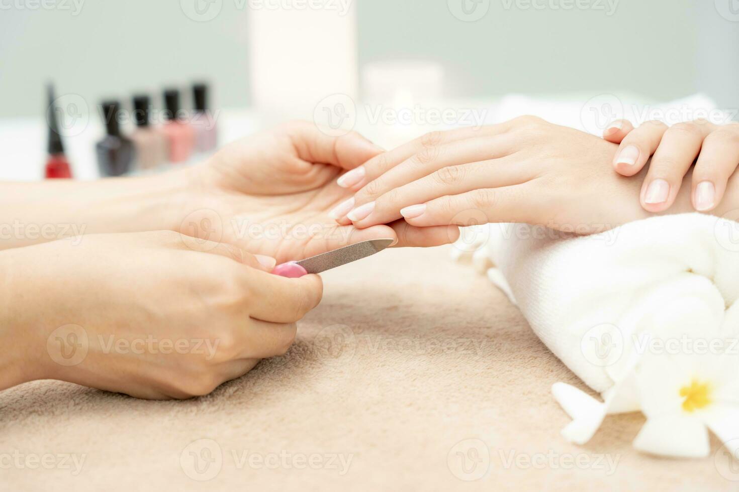 la mujer recibe el servicio de atención de la manicura esteticista profesional en el centro de spa. el salón de belleza de uñas usa una lima de uñas para el tratamiento de acristalamiento. manicurista hace que el cliente de uñas sea hermoso. tratamiento de spa para el cuidado del cuerpo foto