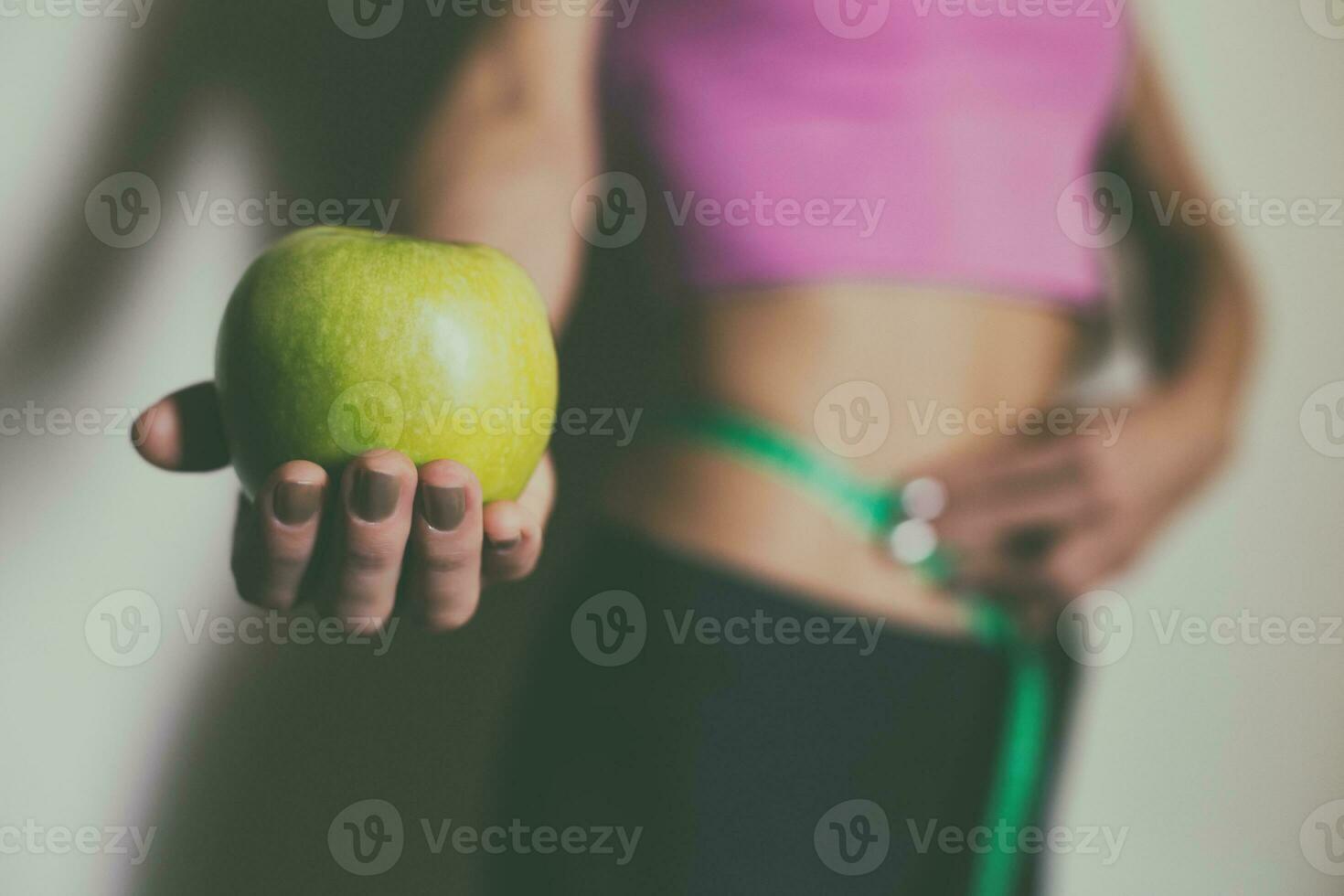Fit woman measuring her thin waist  with a tape measure and holding apple.Focus on apple. photo