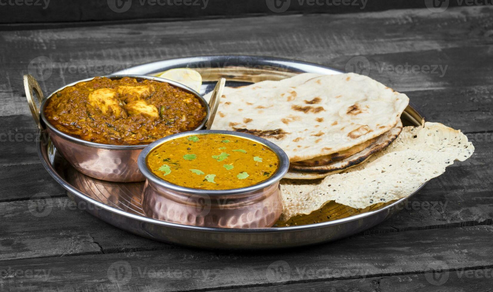 Indian Traditional Thali Food Dal Makhani Served with Chapati, Papad, Kadai Paneer or Lemon on Vintage Wooden Background photo