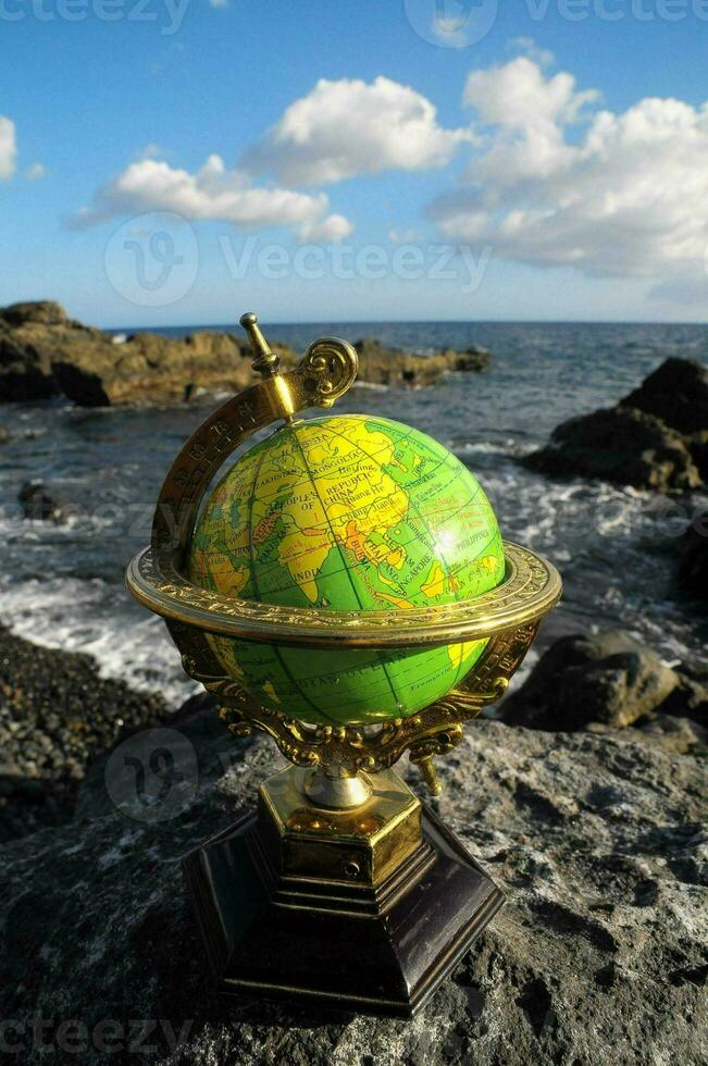 a globe on a rock near the ocean photo