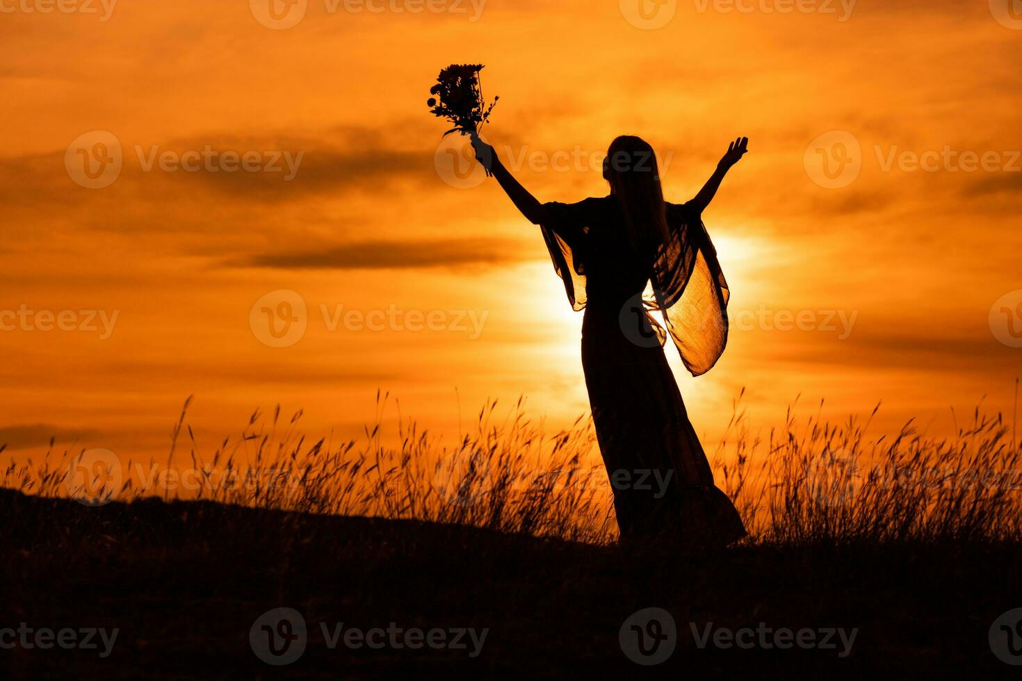 Silhouette of a woman with arms outstretched holding flowers and  looking at beautiful sunset. photo