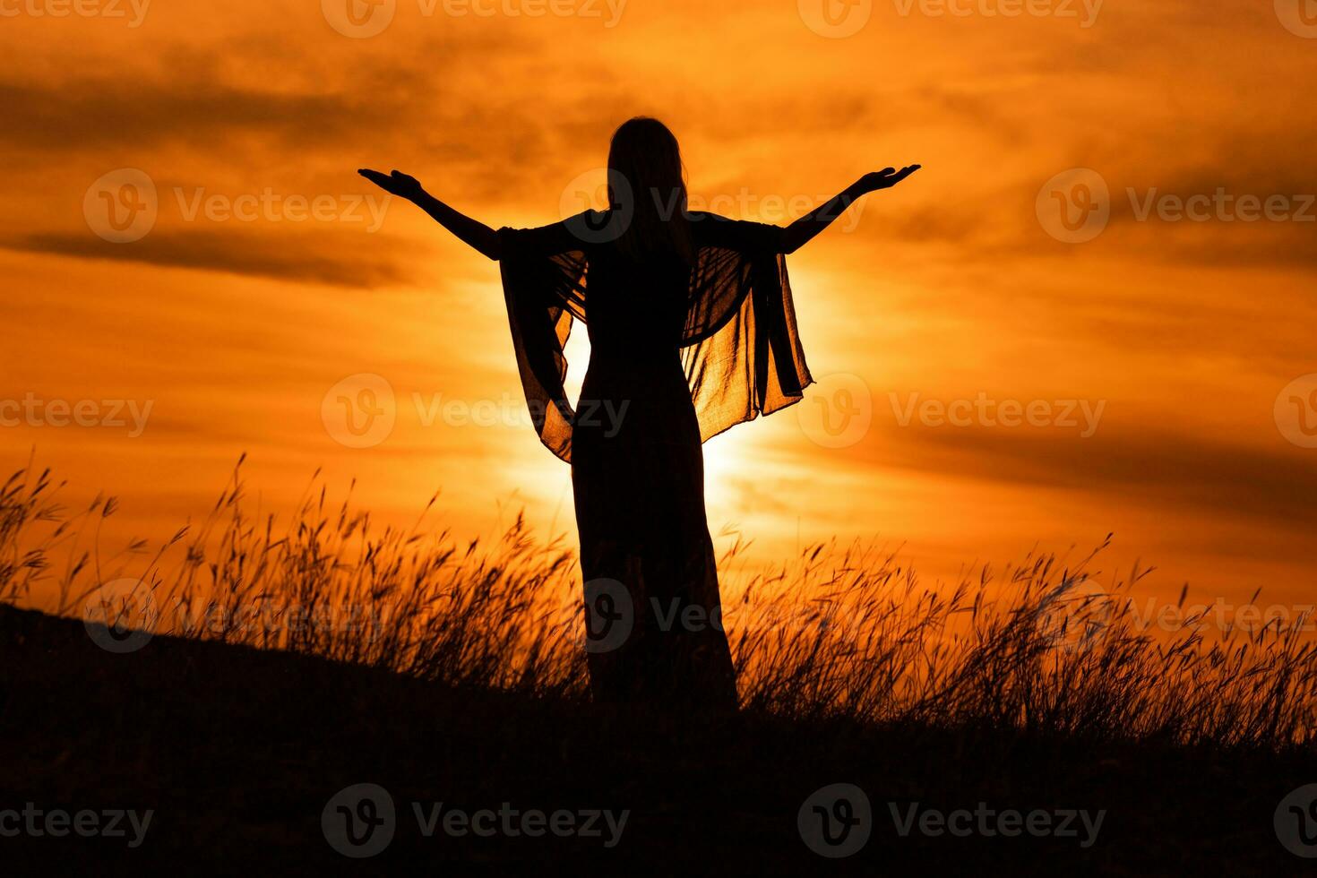 Silhouette of a woman with arms outstretched looking at beautiful sunset. photo