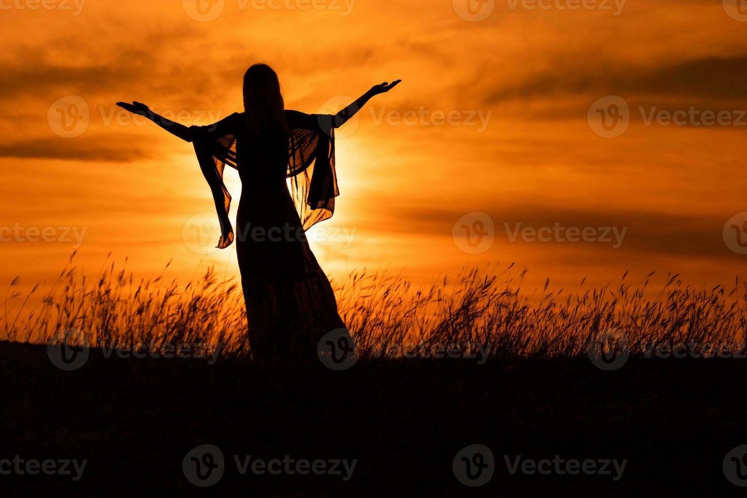 Silhouette of a woman with arms outstretched looking at beautiful sunset. photo