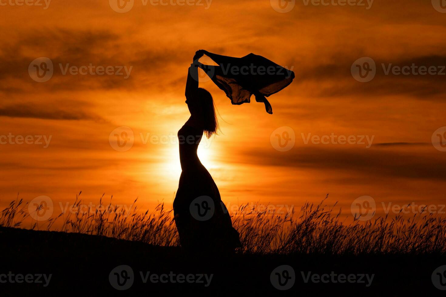 Happy woman dancing and holding scarf while enjoys spending time at sunset. photo