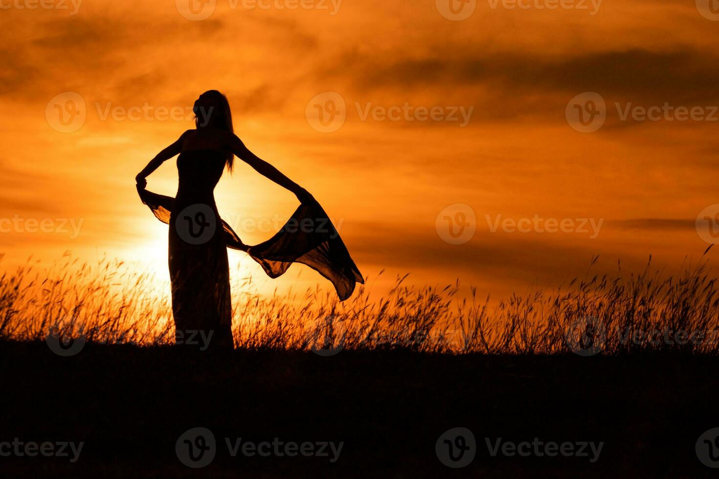 Happy woman dancing and holding scarf while enjoys spending time at sunset. photo