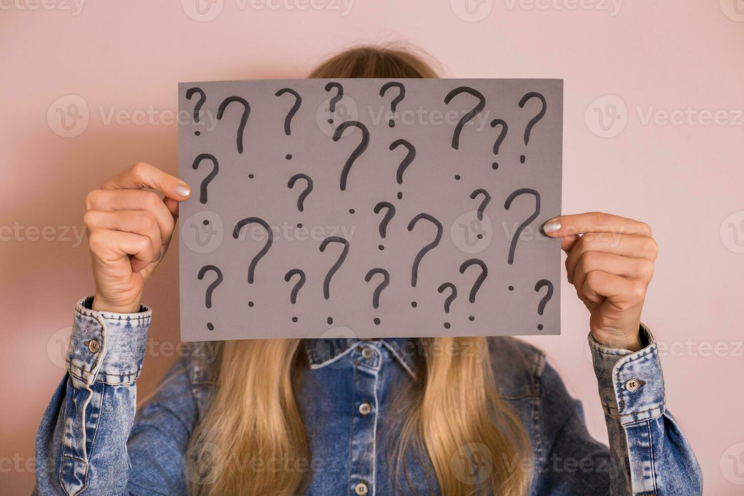 Woman holding paper with question marks while standing in front of the wall. photo