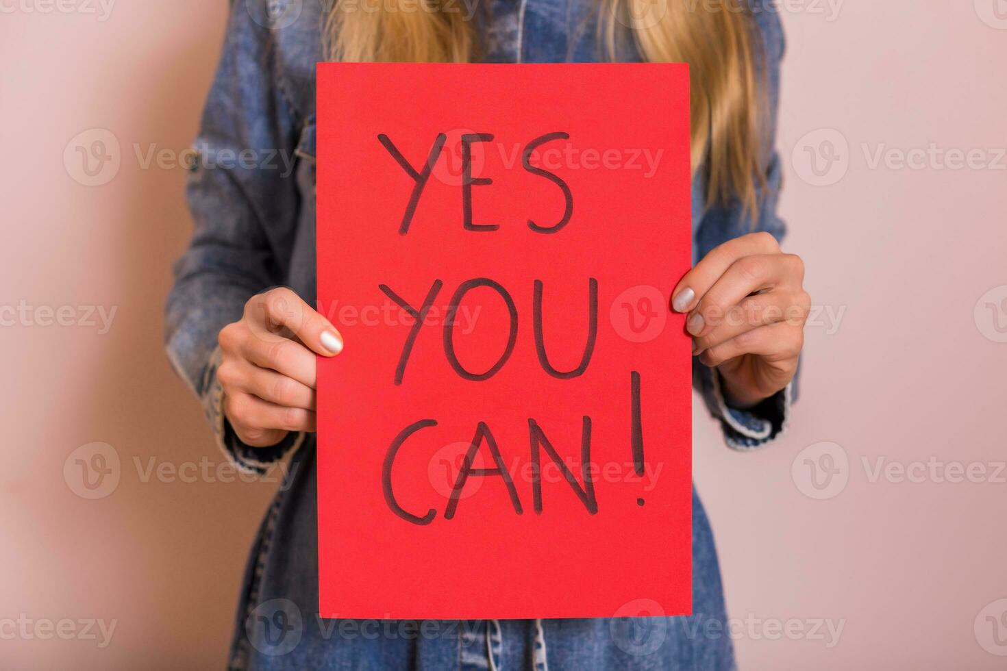 Woman holding paper with text yes you can while standing in front of the wall. photo