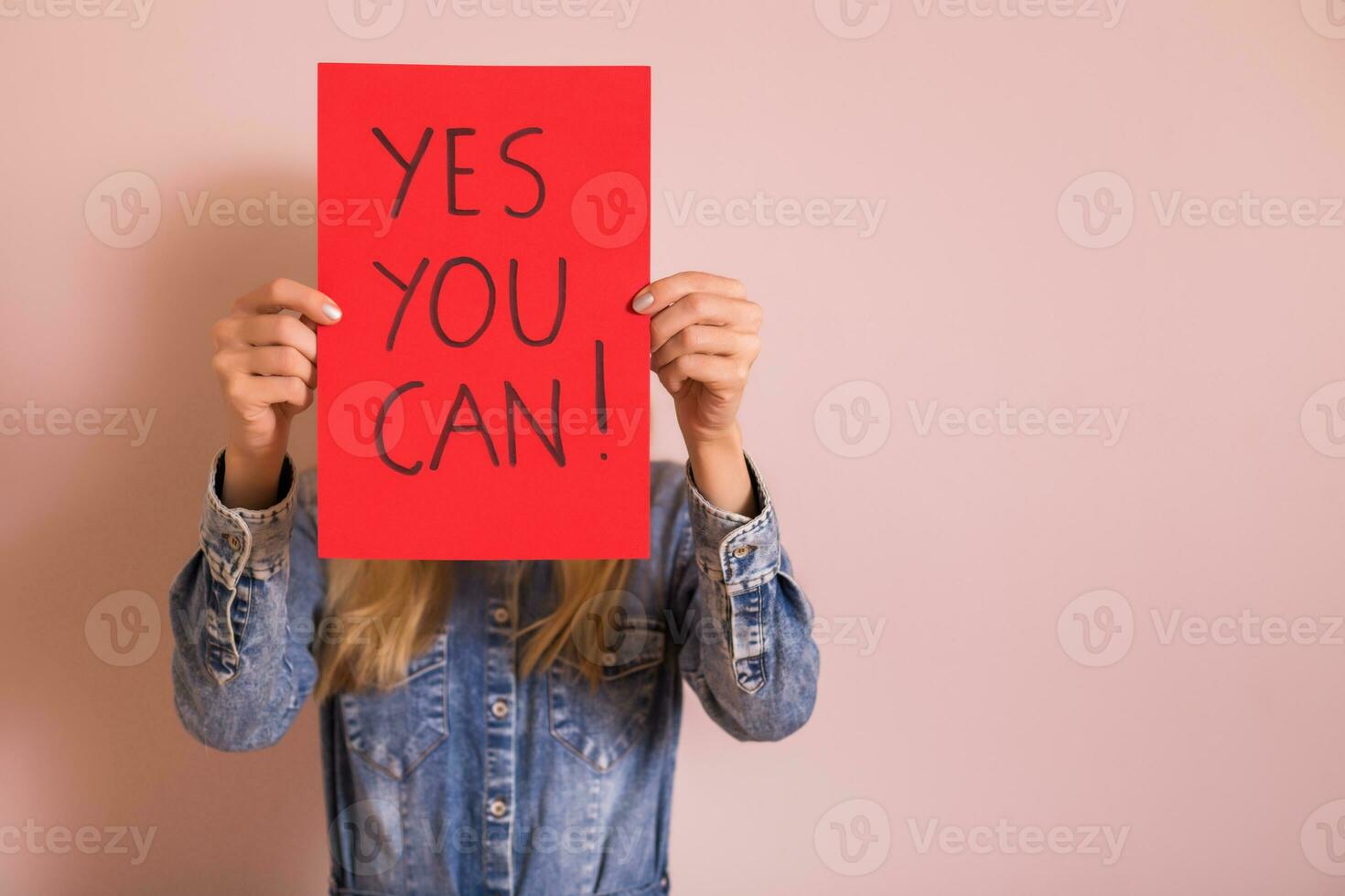 Woman holding paper with text yes you can while standing in front of the wall. photo