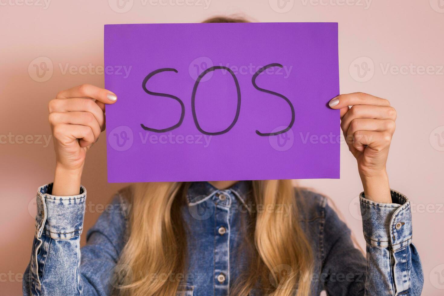 Woman holding paper with word SOS while standing in front of the wall. photo