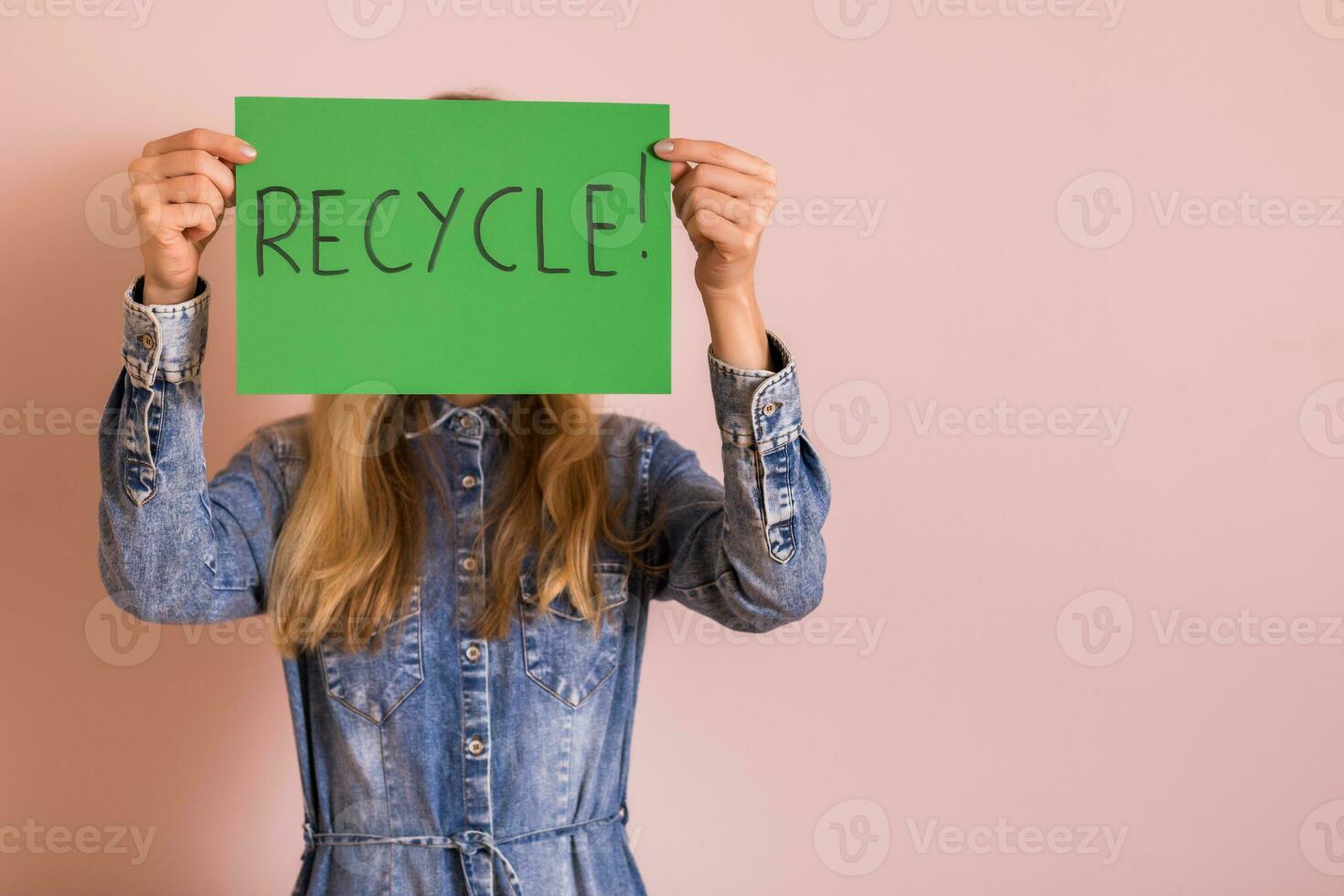 mujer en pie en frente de pared y participación verde papel con palabra reciclar. foto