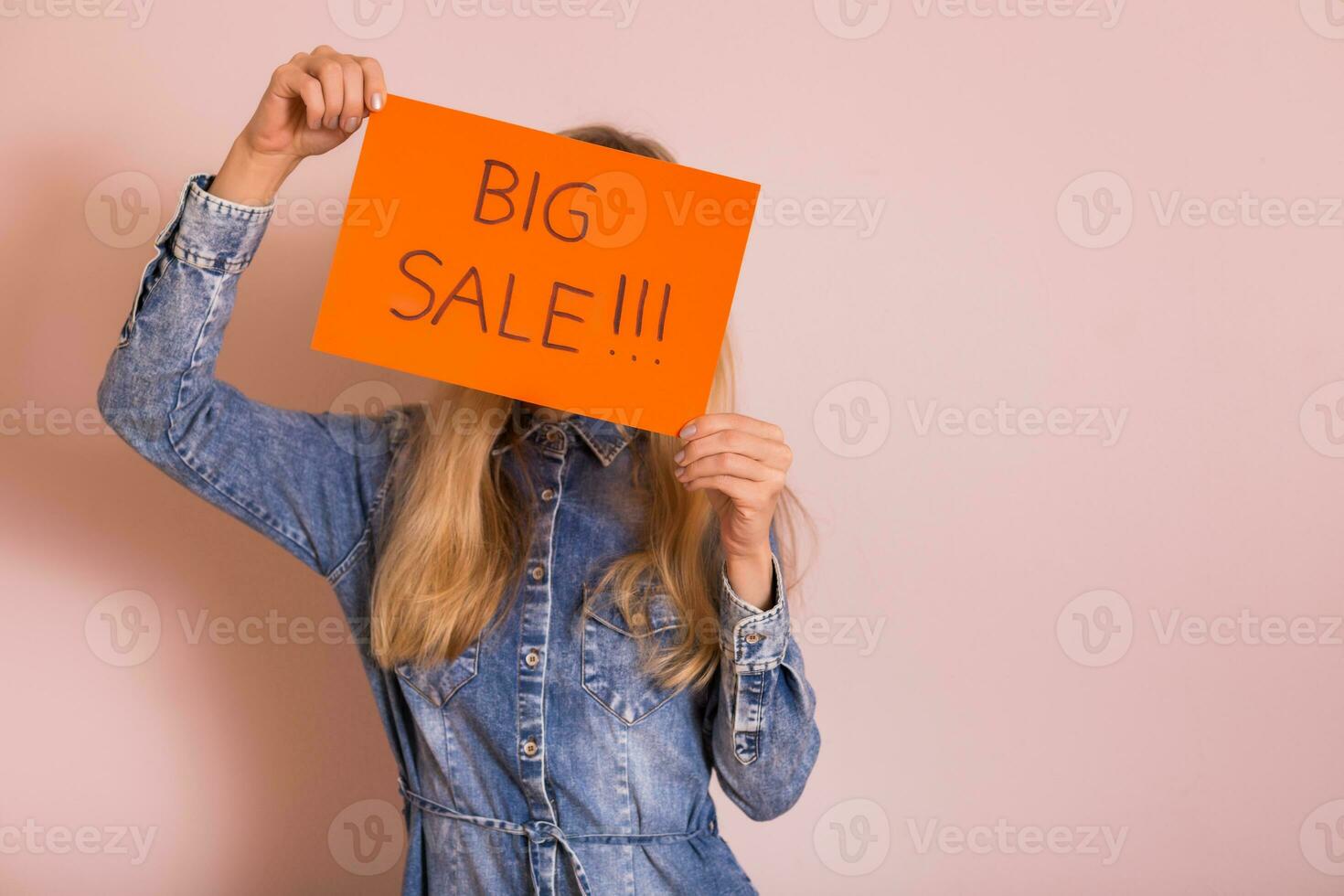 Woman holding paper with text big sale while standing in front of the wall. photo