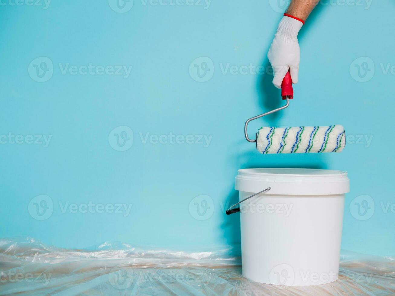 Image of paint can and man holding paint roller in front of blue wall. photo