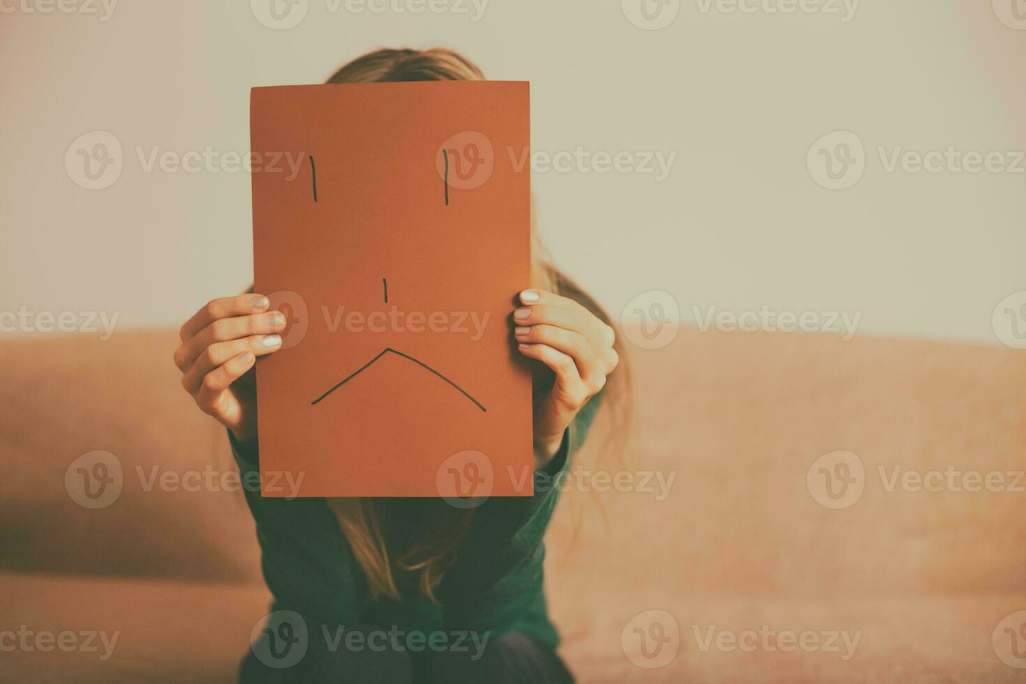 Depressed woman sitting alone at sofa and holding paper with sad face.Toned image. photo