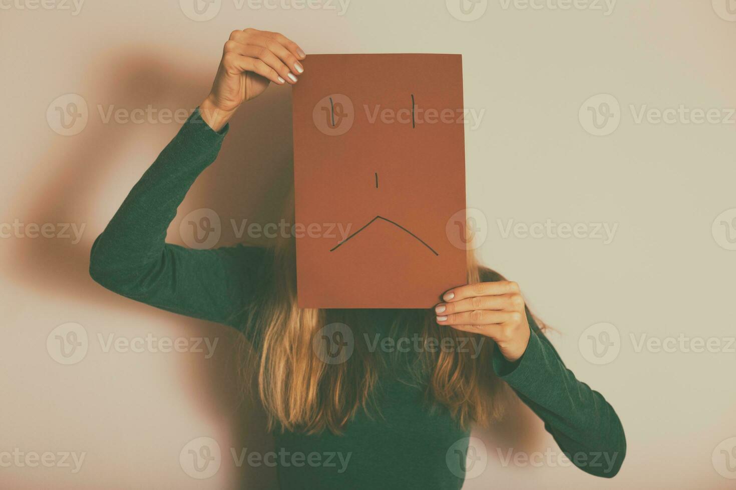 Depressed woman with sad face on paper standing alone in front of wall.Toned image. photo