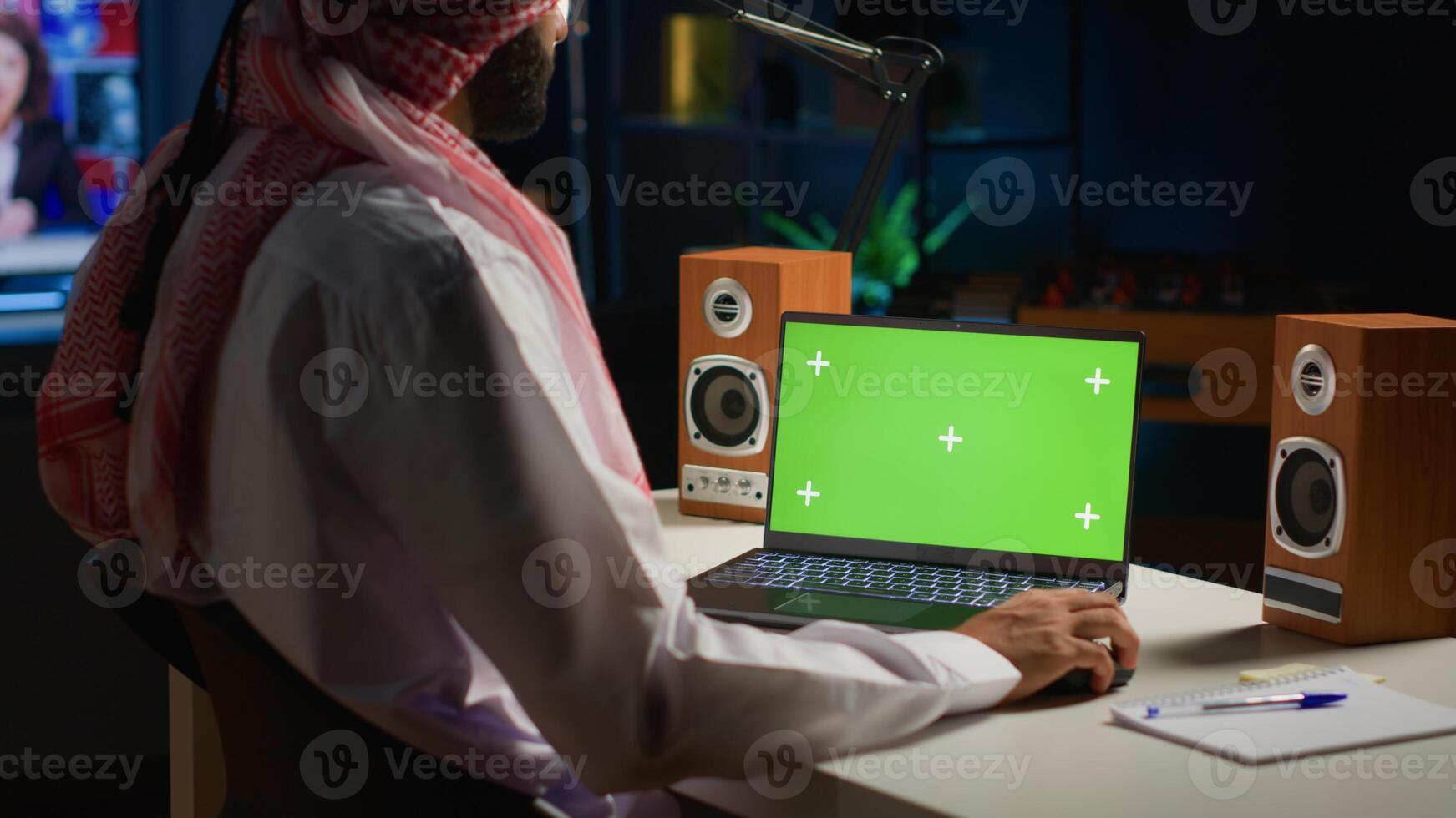 Arabic man scrolling on mockup laptop while working from home. Self employed person writing emails on isolated screen device in apartment office with TV as background noise photo
