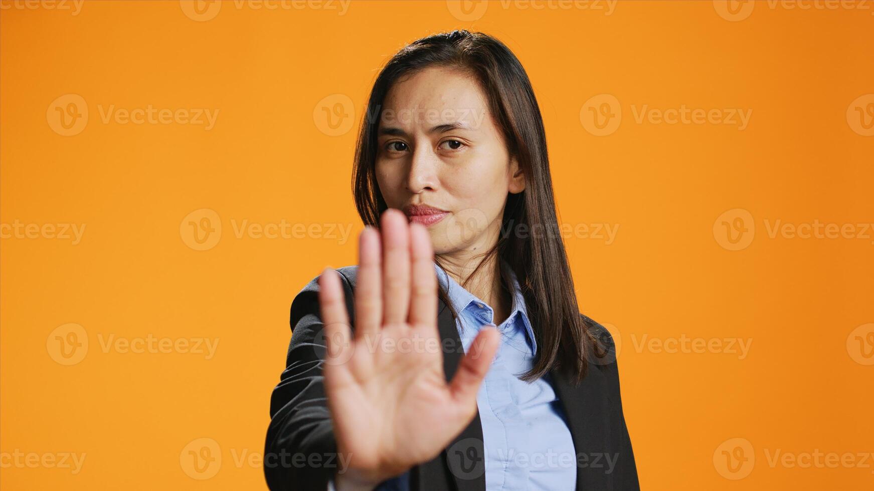 Filipino woman showing stop sign with palm, advertising negativity and no symbol on camera. Female model wearing formal attire in studio, showcasing rejection and refusing something. photo