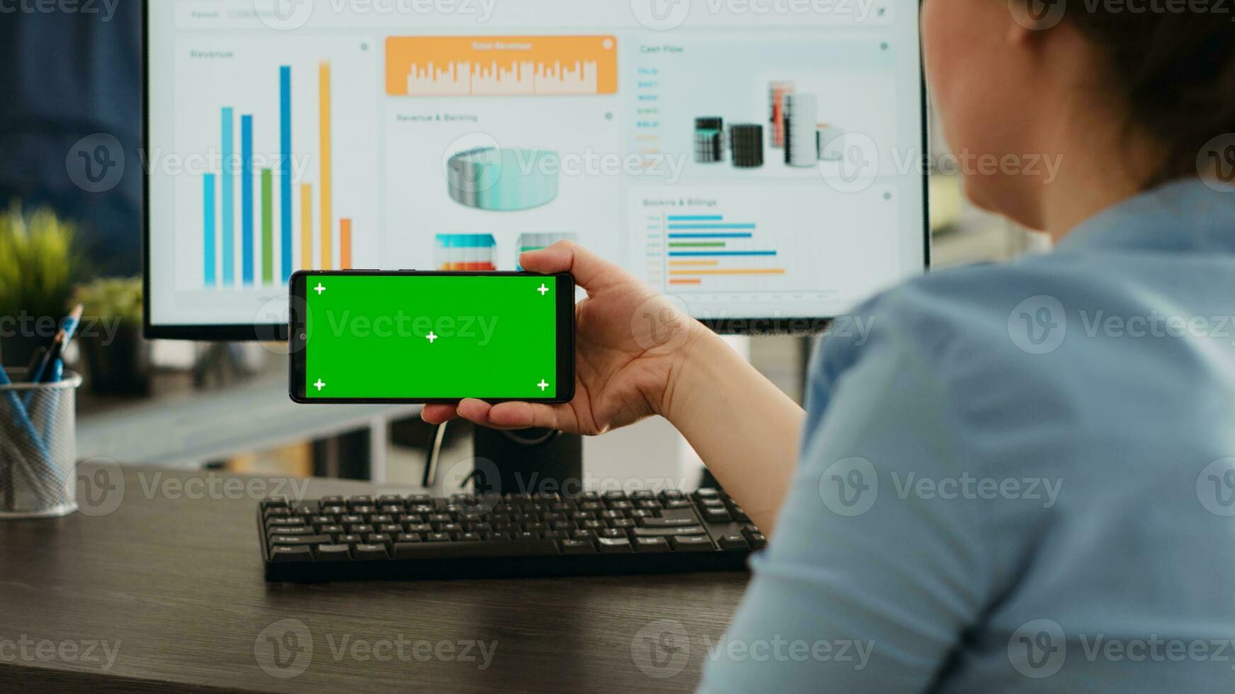 trabajador examina vacío Bosquejo diseño en de moda Teléfono móvil con pantalla verde mostrar. trabajando en teléfono inteligente y computadora a agencia oficina escritorio, analizando móvil software con blanco clave de croma foto