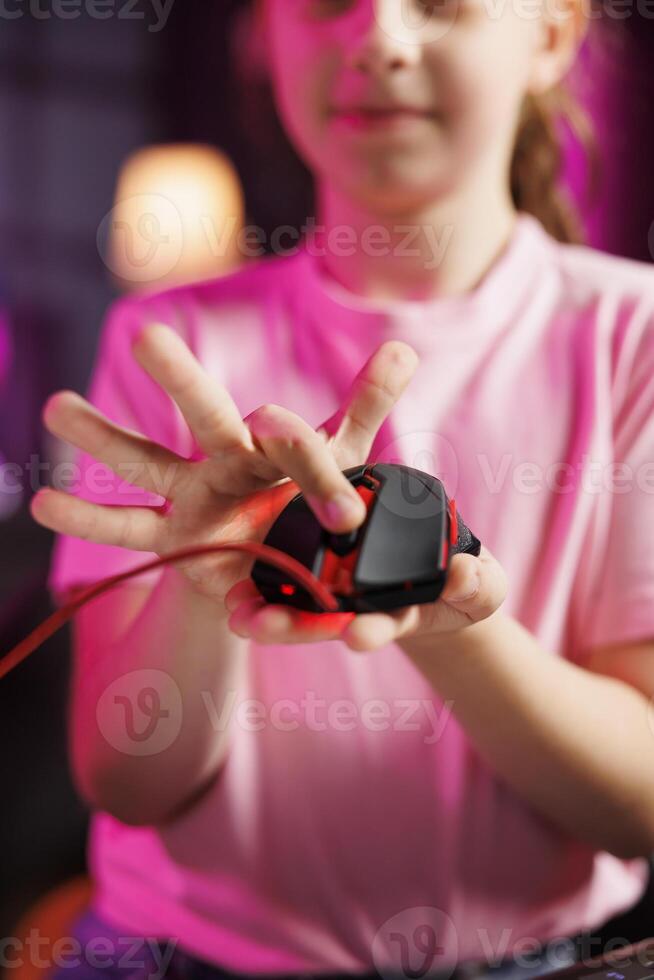 Close up shot of young girl in studio reviewing gaming mouse in front of camera in personal studio. Cheerful kid filming electronics haul, testing scrolling wheel on wired computer peripheral photo