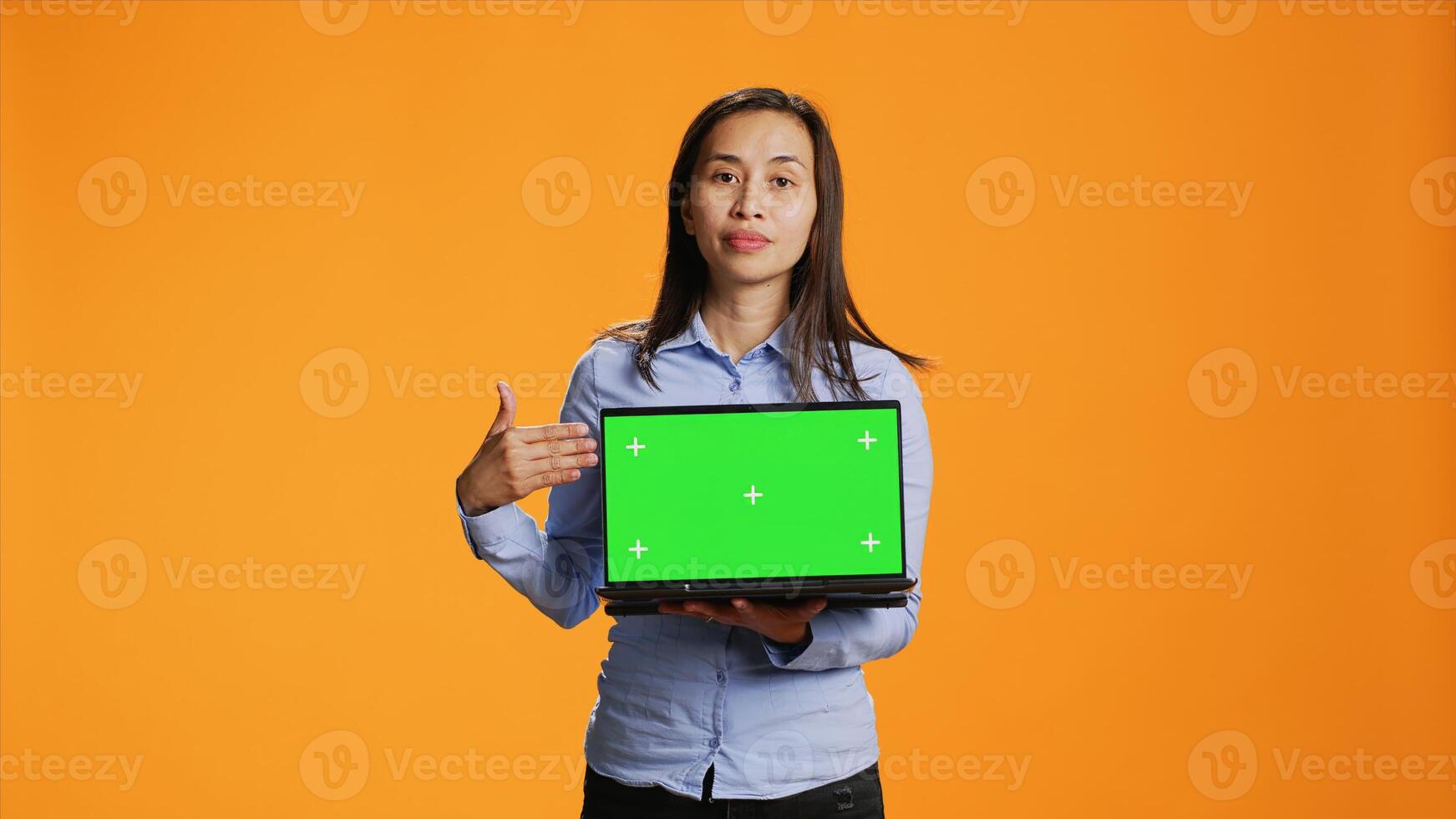 Confident adult showing laptop with greenscreen in studio, presenting isolated mockup template on wireless computer. Asian person holding pc with chromakey display on camera. photo