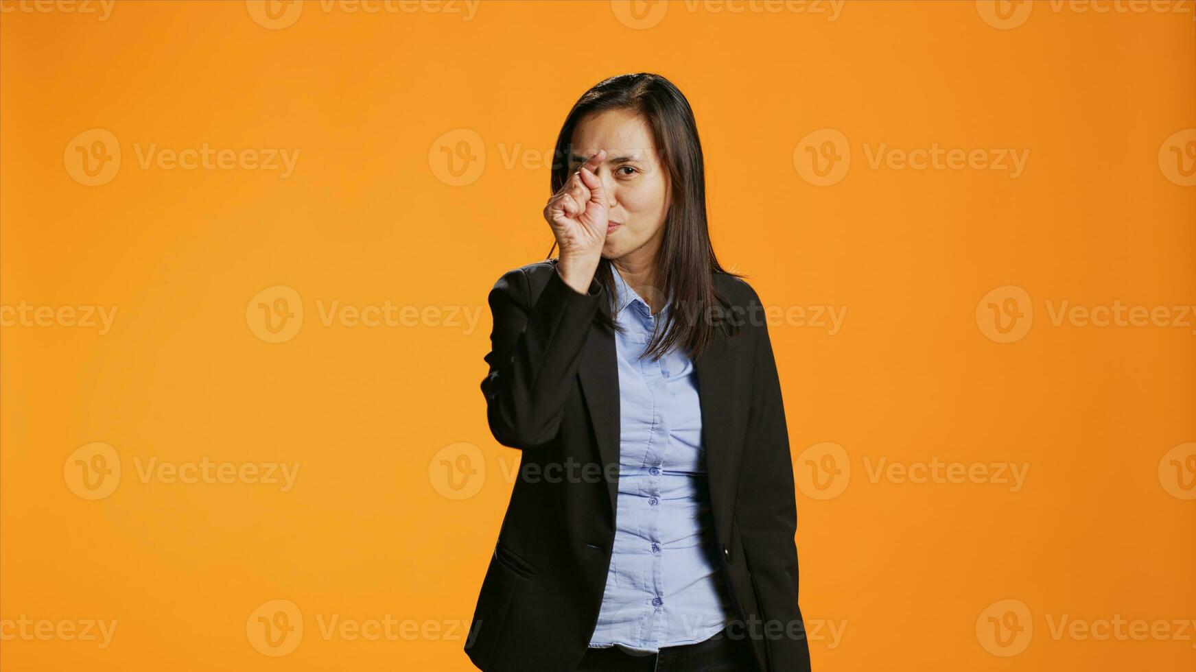 Asian office employee pointing fingers at camera, being serious and confident over orange background. Woman in formal clothes indicates something in front of her, point at the lens. photo