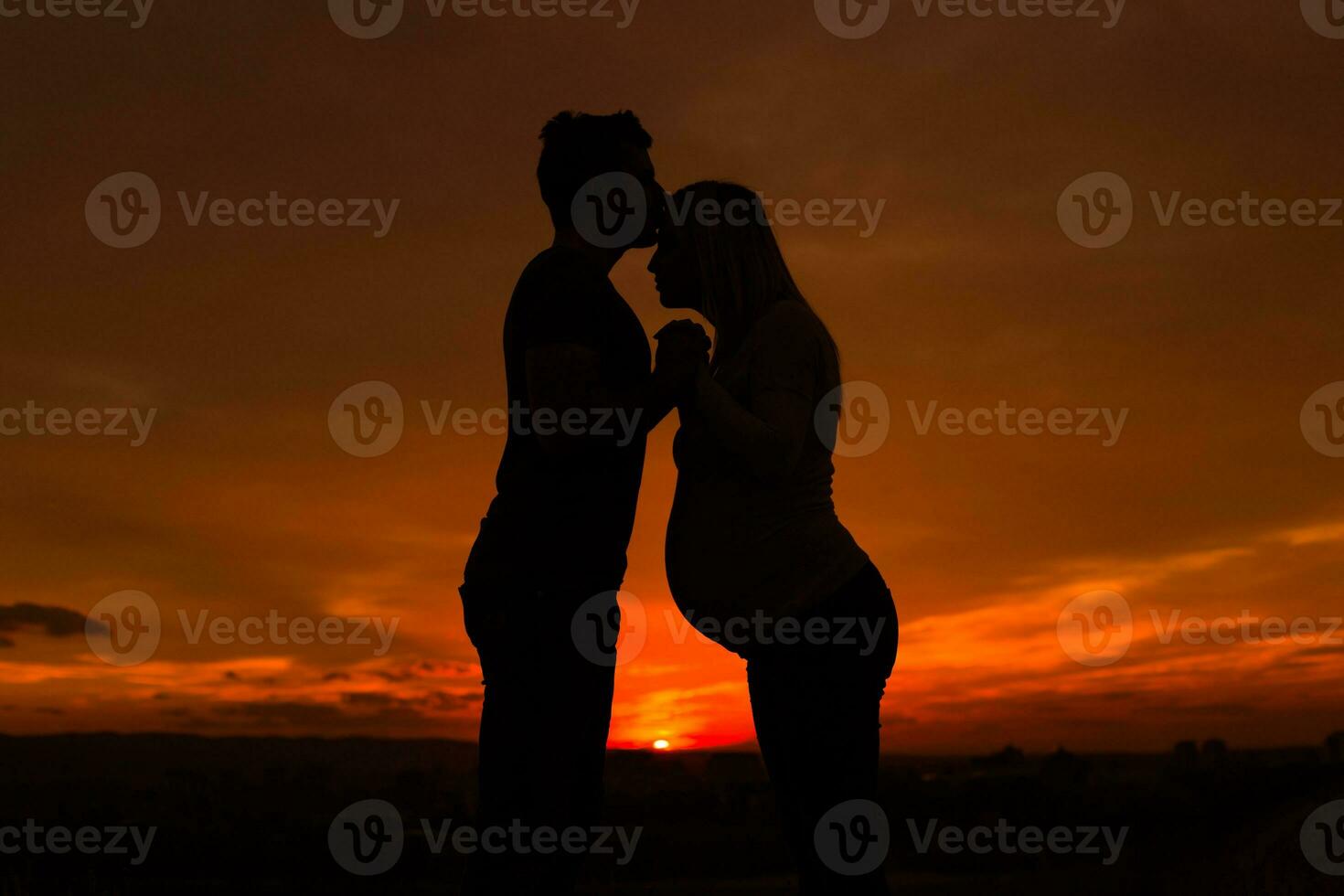 Silhouettes of husband kissing his pregnant wife into forehead and enjoy spending time together outdoor.Toned image. photo