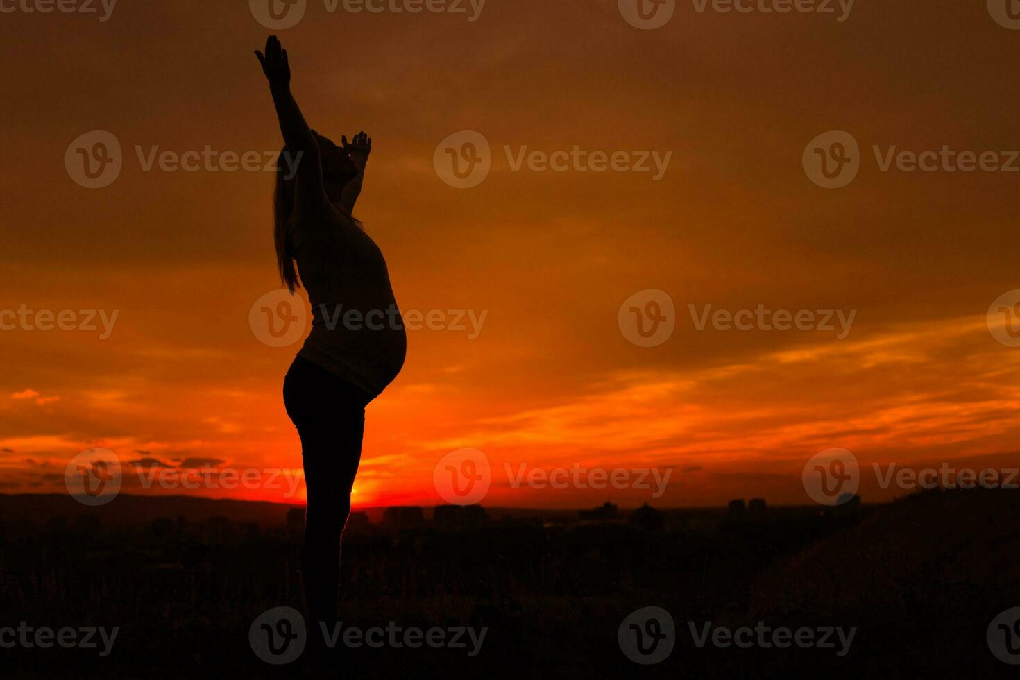 Silhouette of pregnant woman with arms outstretched enjoys spending time outdoor.Toned image. photo