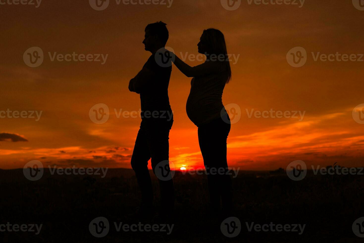 Silhouettes of angry husband and  pregnant wife while they standing outdoor.Toned image. photo