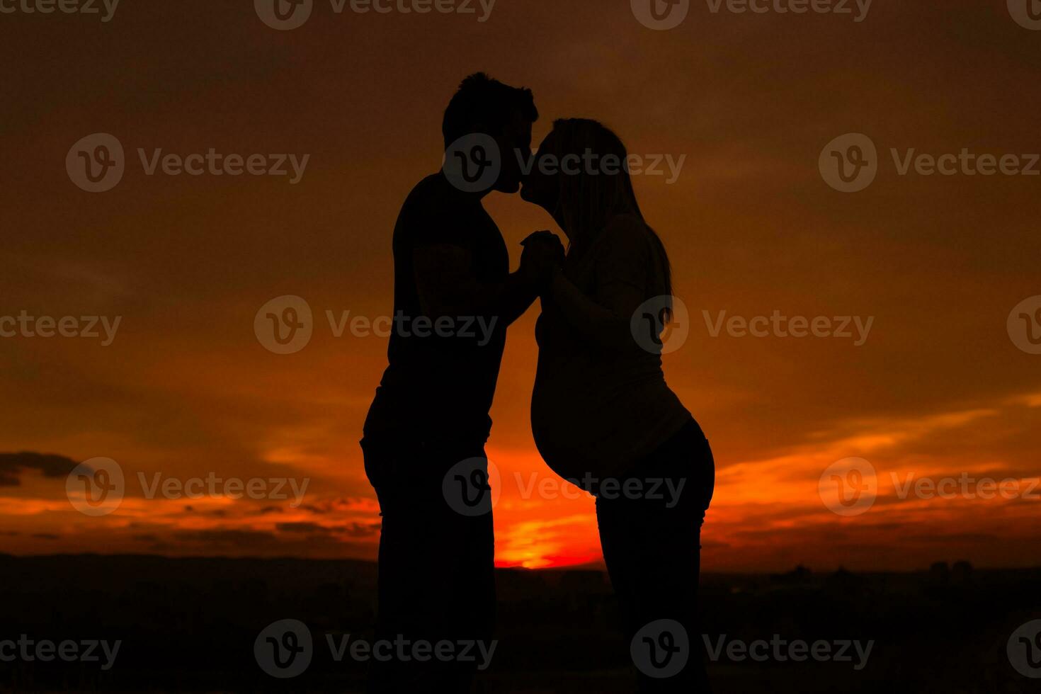 Silhouettes of husband and pregnant wife kissing while they enjoy spending time together outdoor.Toned image. photo