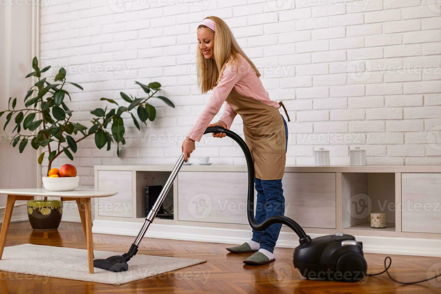 Beautiful housewife cleaning with vacuum cleaner her home. photo