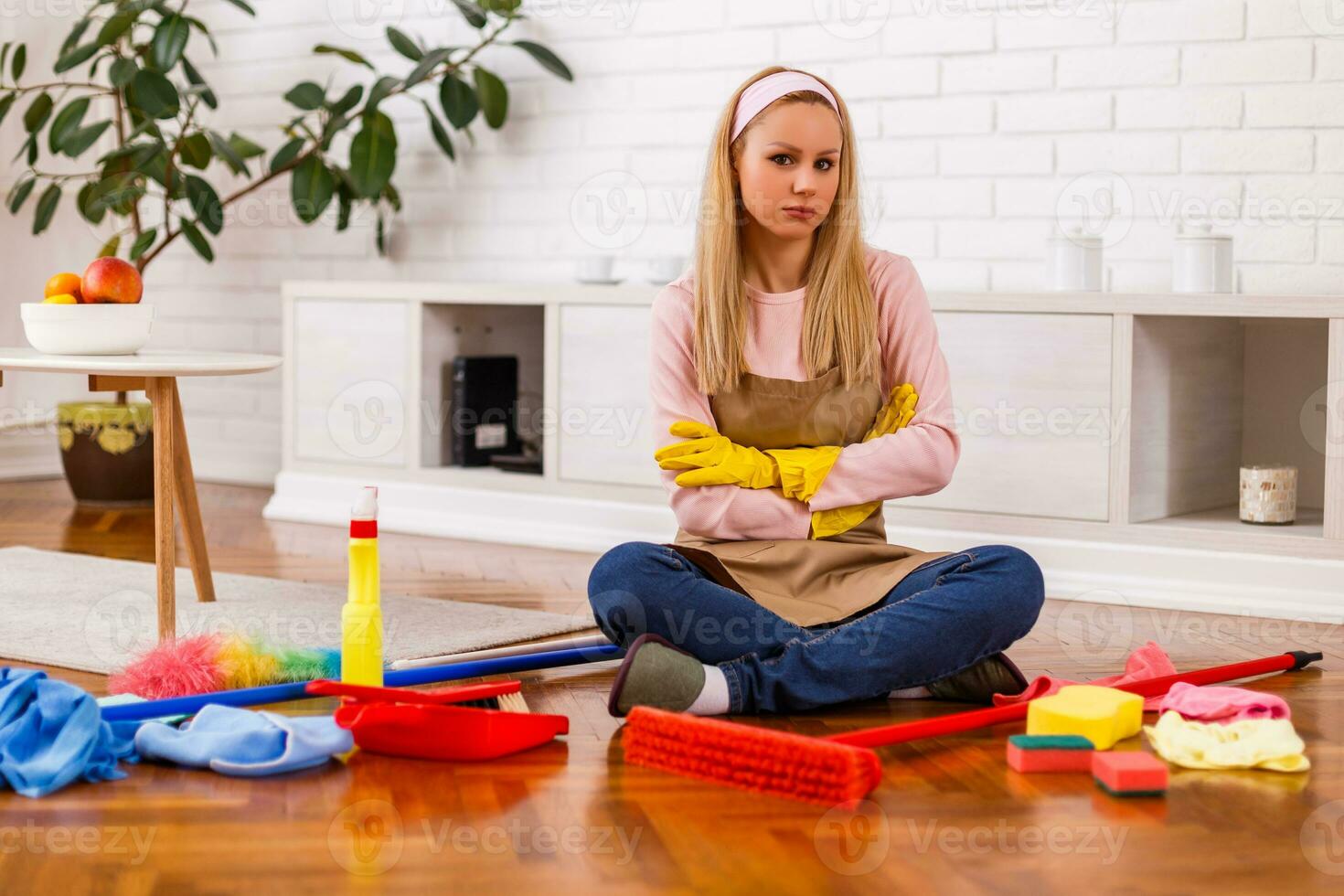 Angry and tired housewife with cleaning equipment sitting in the living room. photo